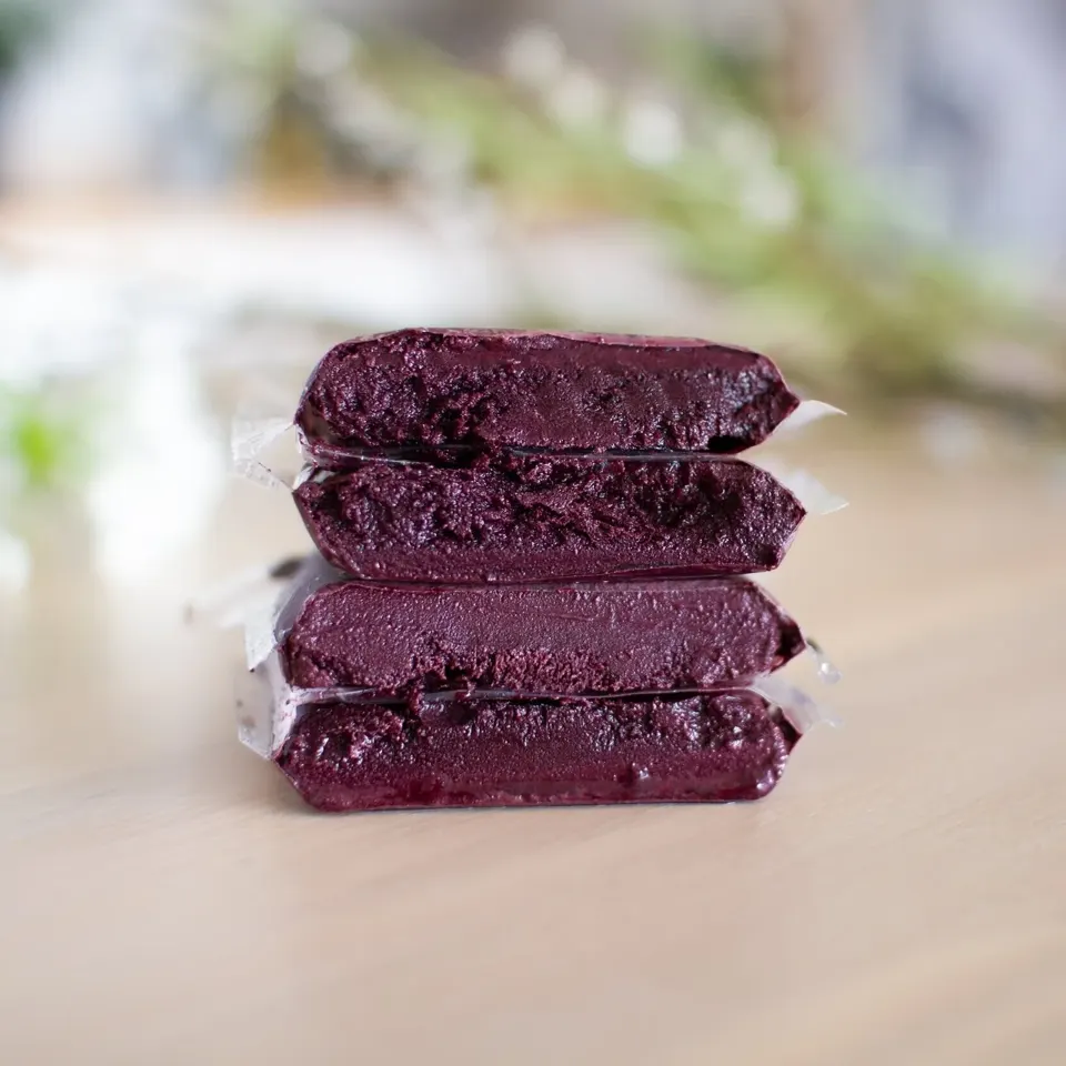 Fire frosne 100 g breve med mørklilla açaí-puré stablet på et bord